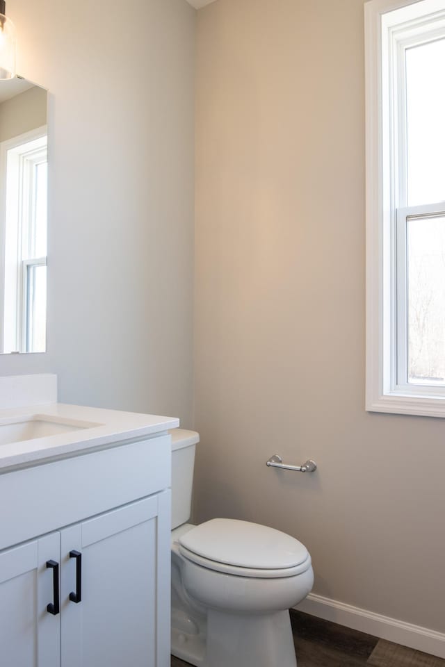 half bath with wood finished floors, vanity, toilet, and baseboards