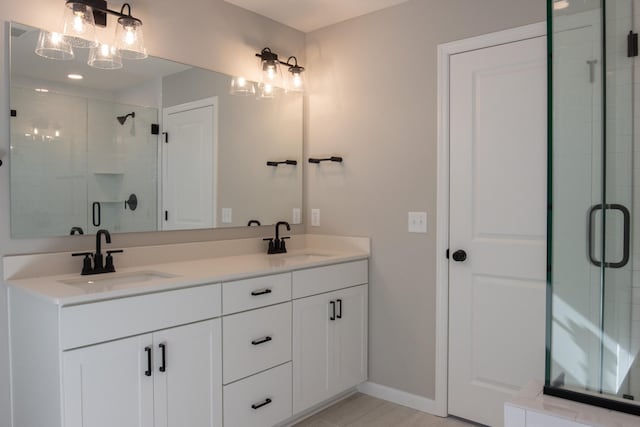 full bathroom featuring double vanity, a shower stall, baseboards, and a sink