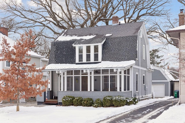 dutch colonial featuring a detached garage, a sunroom, a gambrel roof, a chimney, and roof with shingles