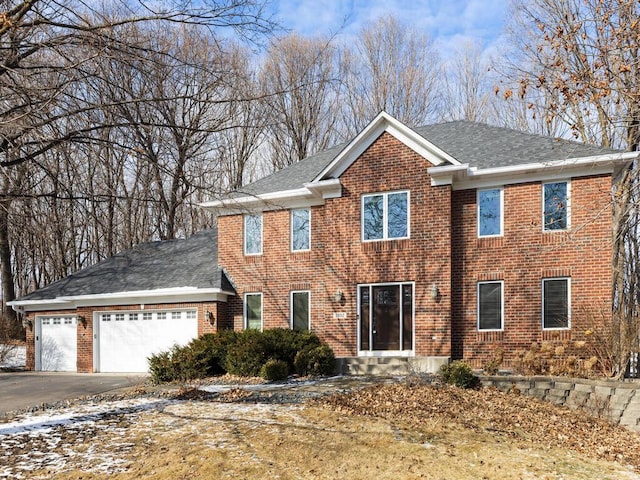 colonial-style house featuring brick siding, driveway, an attached garage, and roof with shingles