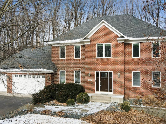 colonial home featuring a shingled roof, brick siding, driveway, and a garage