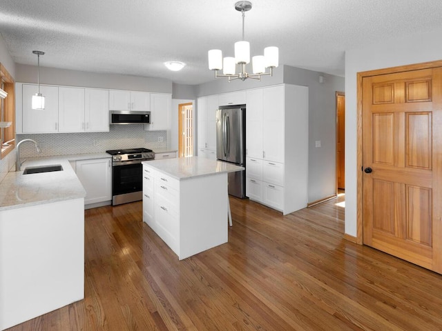 kitchen with stainless steel appliances, a sink, white cabinetry, a center island, and decorative light fixtures