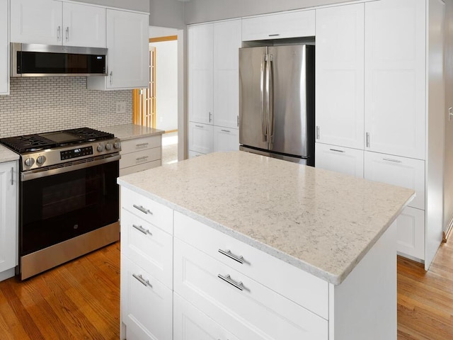 kitchen with stainless steel appliances, light wood finished floors, white cabinetry, and a center island