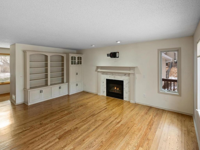 unfurnished living room featuring light wood finished floors, baseboards, a textured ceiling, and a high end fireplace