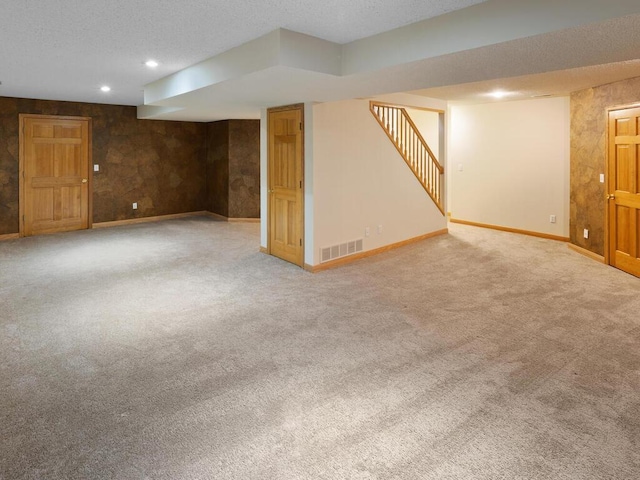 finished below grade area featuring stairs, carpet flooring, visible vents, and baseboards