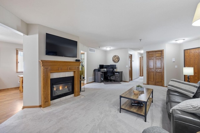 living area with light carpet, a tiled fireplace, and visible vents