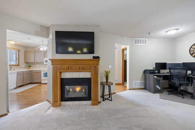 office area featuring light carpet, a fireplace, visible vents, and a textured ceiling