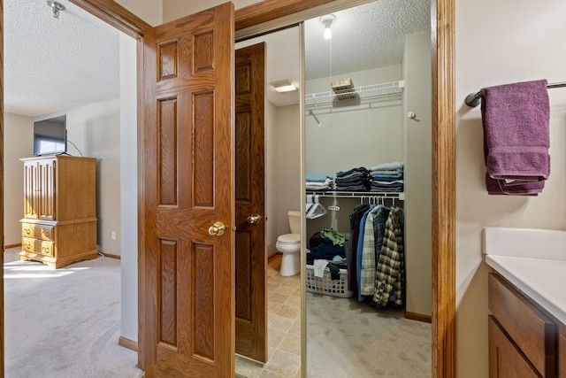 bathroom with a spacious closet, toilet, a textured ceiling, vanity, and baseboards