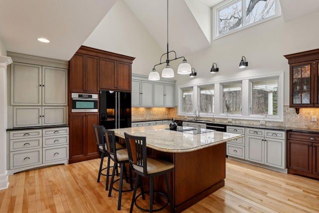 kitchen featuring sink, light stone counters, a center island, hanging light fixtures, and black appliances