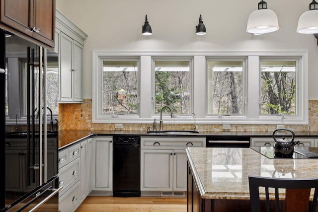 kitchen featuring sink, dark stone countertops, hanging light fixtures, tasteful backsplash, and black appliances