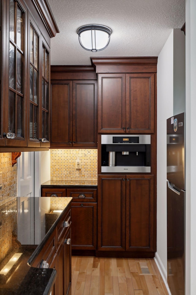 kitchen with dark stone countertops, backsplash, oven, light hardwood / wood-style floors, and a textured ceiling