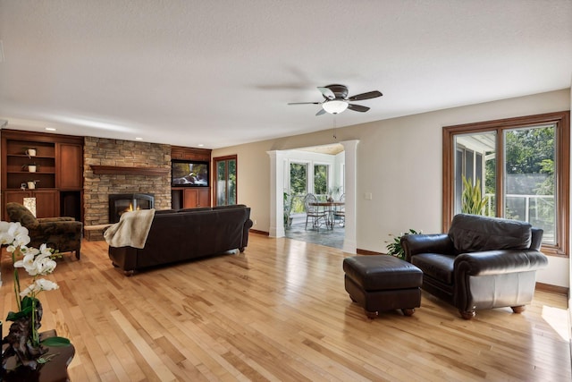 living room with a stone fireplace, a wealth of natural light, ceiling fan, and light wood-type flooring