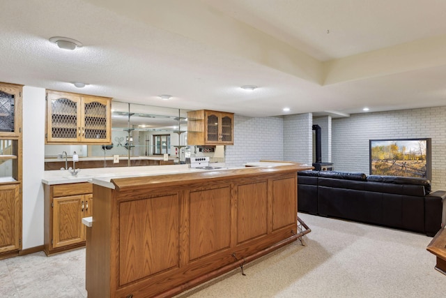 kitchen with brick wall, a wood stove, sink, hanging light fixtures, and kitchen peninsula