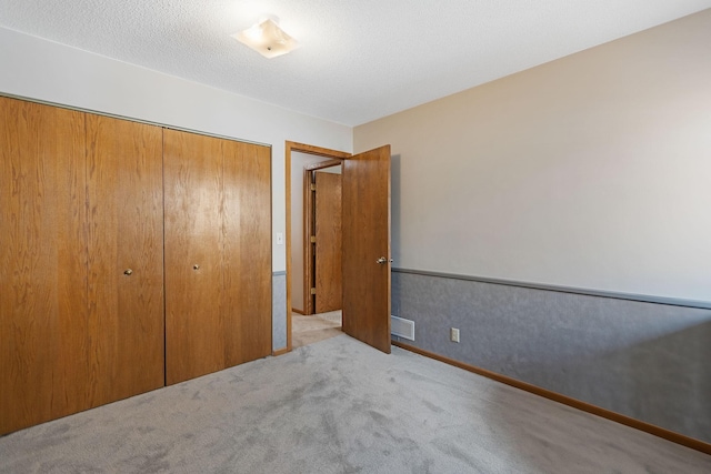 unfurnished bedroom with light colored carpet, a textured ceiling, and a closet