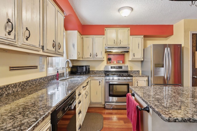 kitchen featuring sink, dark stone counters, black appliances, cream cabinets, and light wood-type flooring