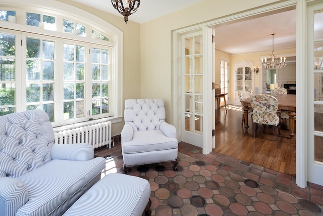 living area featuring radiator, a notable chandelier, french doors, and a healthy amount of sunlight