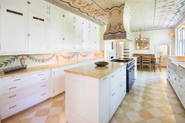 kitchen with high end stove, white cabinets, a kitchen island, decorative light fixtures, and custom exhaust hood