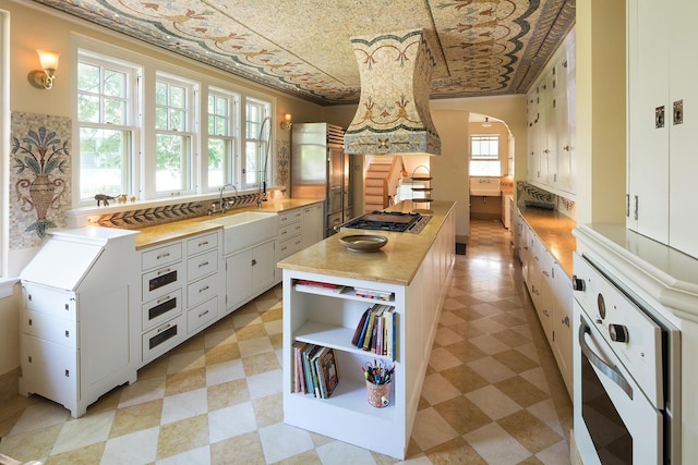 kitchen with sink, white oven, white cabinetry, ornamental molding, and stainless steel gas stovetop