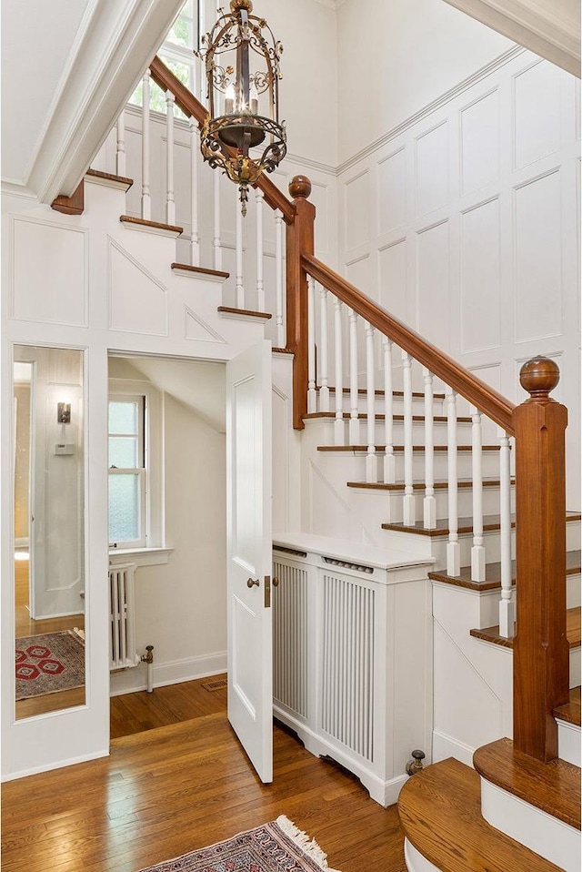 stairs with radiator, hardwood / wood-style flooring, and a notable chandelier