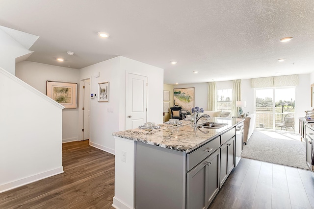 kitchen featuring sink, dark hardwood / wood-style flooring, gray cabinets, an island with sink, and light stone countertops