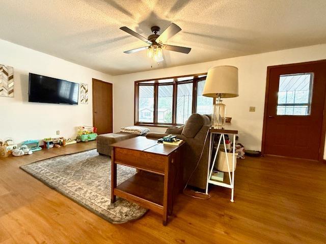 living area with a textured ceiling, ceiling fan, and wood finished floors