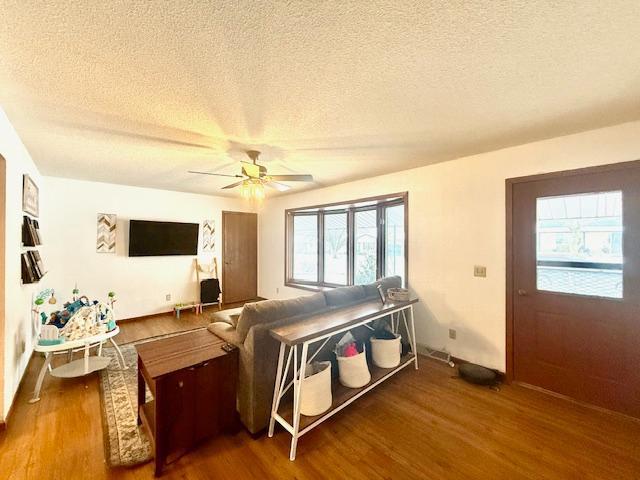 living area featuring baseboards, a textured ceiling, ceiling fan, and wood finished floors