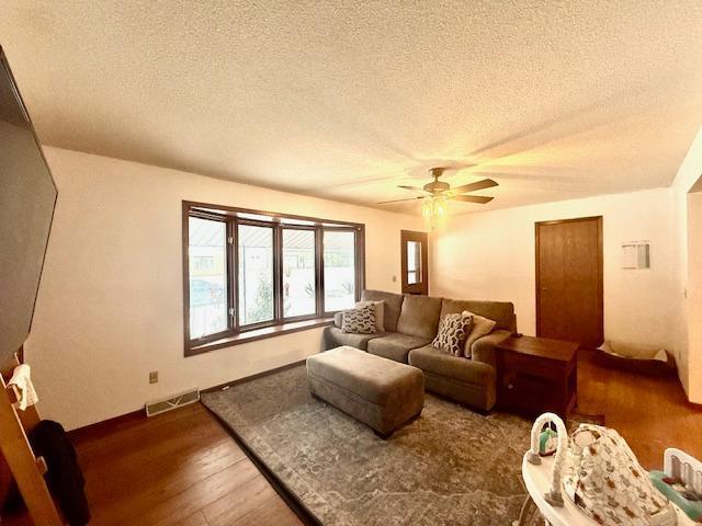 living room featuring visible vents, a ceiling fan, a textured ceiling, and wood finished floors