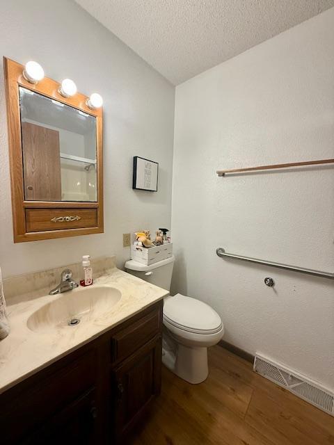 bathroom with a textured ceiling, visible vents, wood finished floors, vanity, and toilet