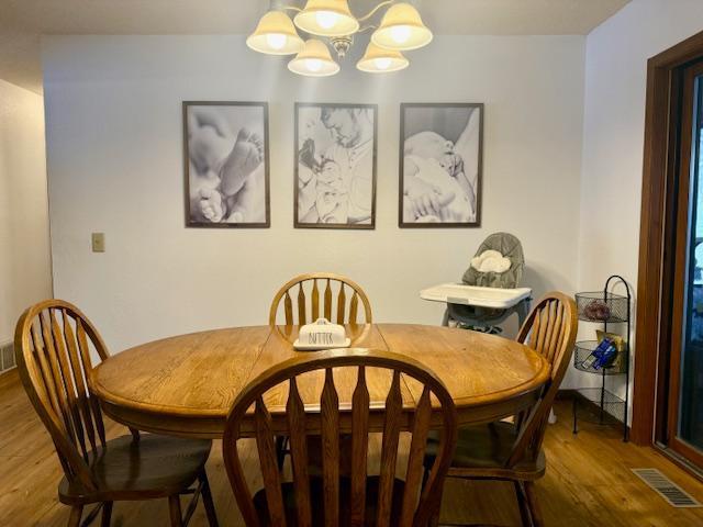 dining space with visible vents, wood finished floors, and an inviting chandelier