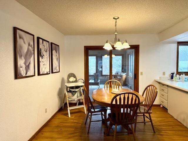 dining area featuring a textured ceiling, wood finished floors, a chandelier, and a healthy amount of sunlight