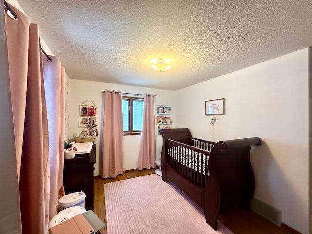 bedroom with visible vents, a crib, a textured ceiling, and wood finished floors