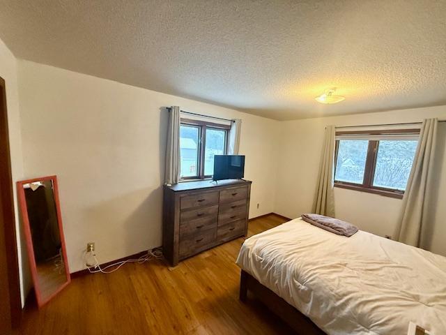 bedroom featuring a textured ceiling, multiple windows, and wood finished floors
