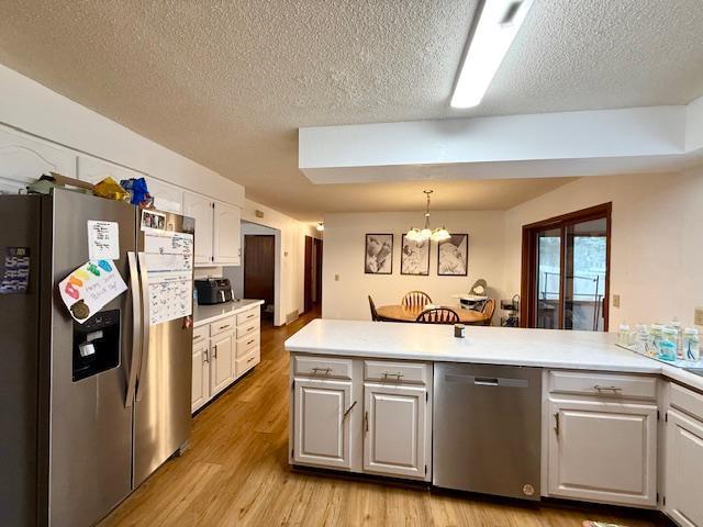 kitchen with stainless steel appliances, a textured ceiling, an inviting chandelier, and light wood-style floors