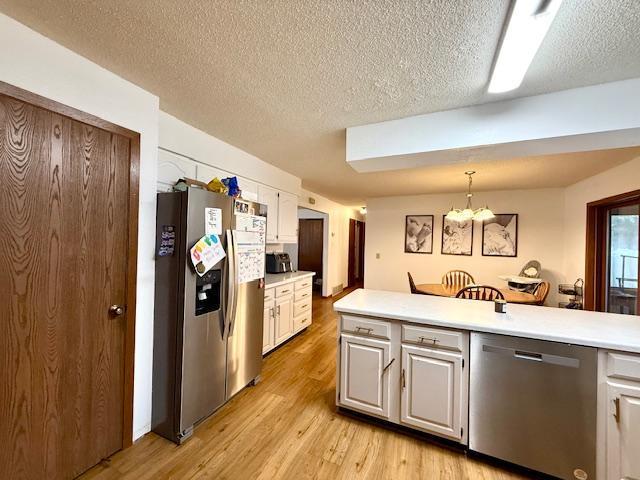 kitchen featuring light wood-style floors, a textured ceiling, appliances with stainless steel finishes, light countertops, and an inviting chandelier