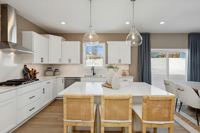 kitchen with sink, stainless steel appliances, a kitchen island, decorative light fixtures, and wall chimney exhaust hood