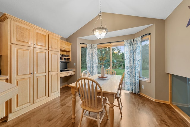 dining area with vaulted ceiling, built in desk, and light hardwood / wood-style floors