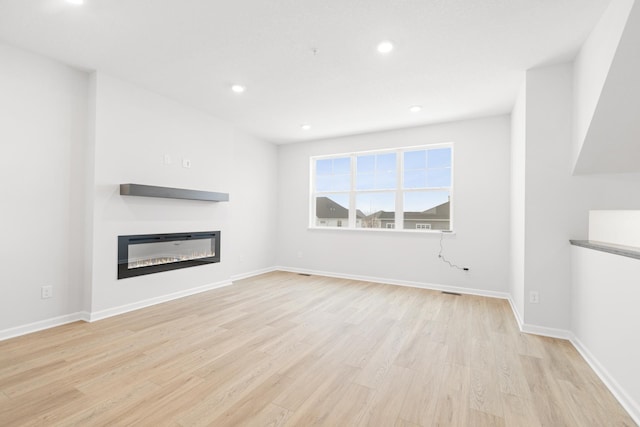 unfurnished living room with light wood-type flooring, a glass covered fireplace, baseboards, and recessed lighting