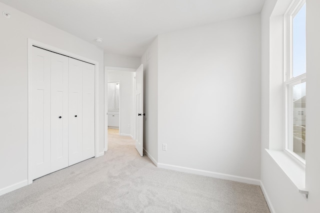 unfurnished bedroom with a closet, light carpet, and baseboards