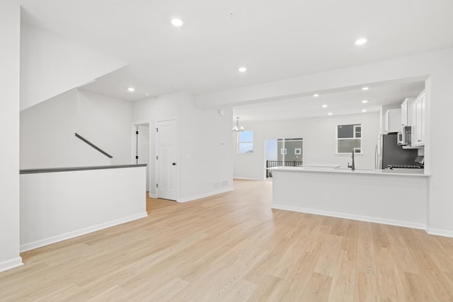 unfurnished living room with a chandelier, light wood-type flooring, baseboards, and recessed lighting