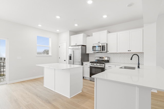 kitchen with stainless steel appliances, a kitchen island, a sink, white cabinets, and light countertops