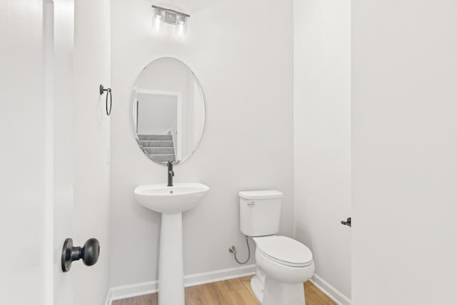 half bath featuring a sink, wood finished floors, toilet, and baseboards