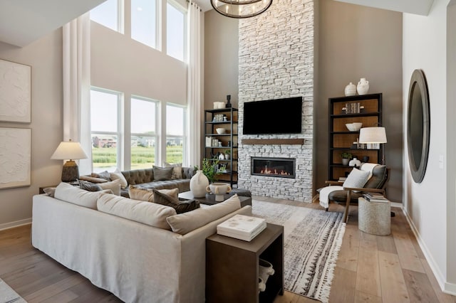 living room featuring a towering ceiling, a stone fireplace, and light hardwood / wood-style floors