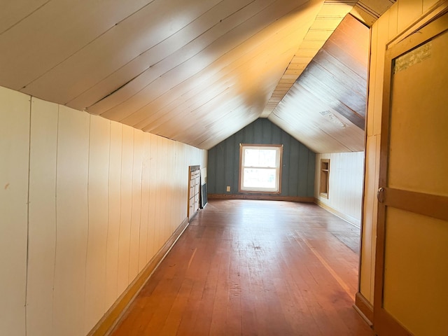 additional living space with wood-type flooring, lofted ceiling, and wooden walls