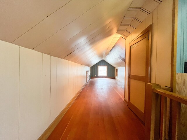 corridor featuring wood-type flooring, wooden walls, and vaulted ceiling