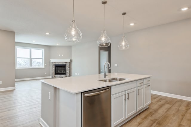 kitchen with pendant lighting, sink, dishwasher, white cabinetry, and a center island with sink