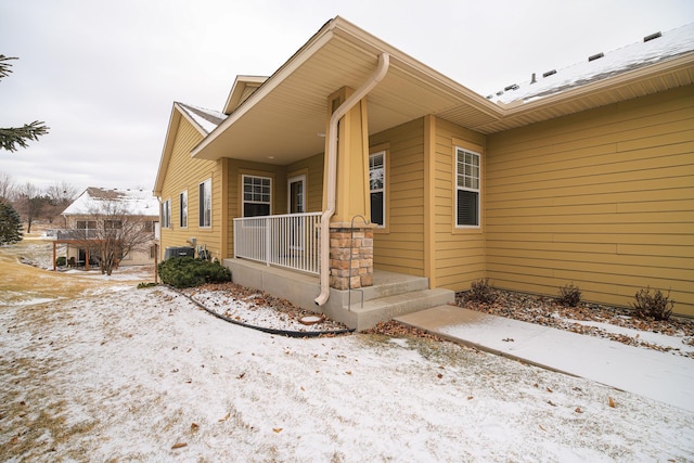 view of snow covered exterior with central AC and covered porch