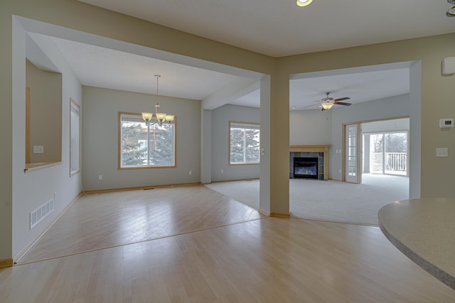 unfurnished living room with a tile fireplace, plenty of natural light, ceiling fan with notable chandelier, and light hardwood / wood-style floors