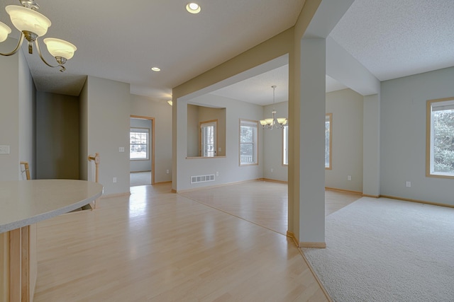 unfurnished living room with a chandelier, a textured ceiling, and light wood-type flooring