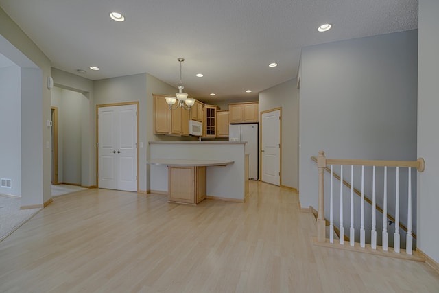 kitchen with light brown cabinetry, decorative light fixtures, a center island, light hardwood / wood-style flooring, and white appliances