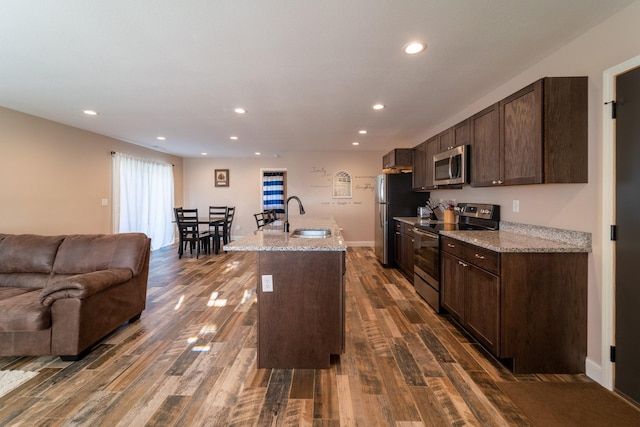 kitchen with open floor plan, stainless steel appliances, dark brown cabinets, and a sink